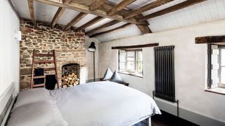 Contemporary cottage style bedroom with bare brick wall, ceiling beams, bed with white linen, black designer radiator and lime plaster walls