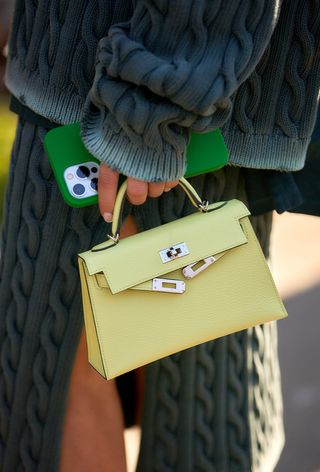 a close-up photo of a woman carrying a small yellow Hermes bag and an iPhone