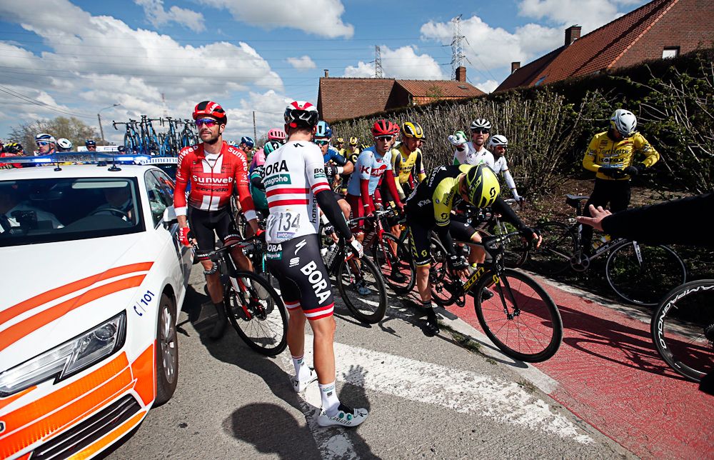 Riders wait as officials temporarily stop Dwars door Vlaanderen