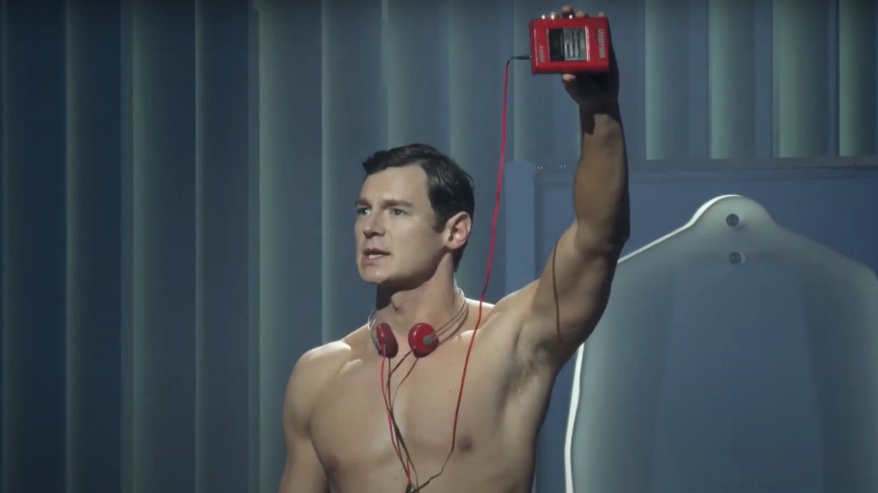 A shirtless Benjamin Walker proudly holds up a red Walkman in American Psycho: The Musical.