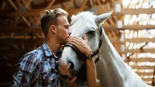 man hugging and kissing grey horse