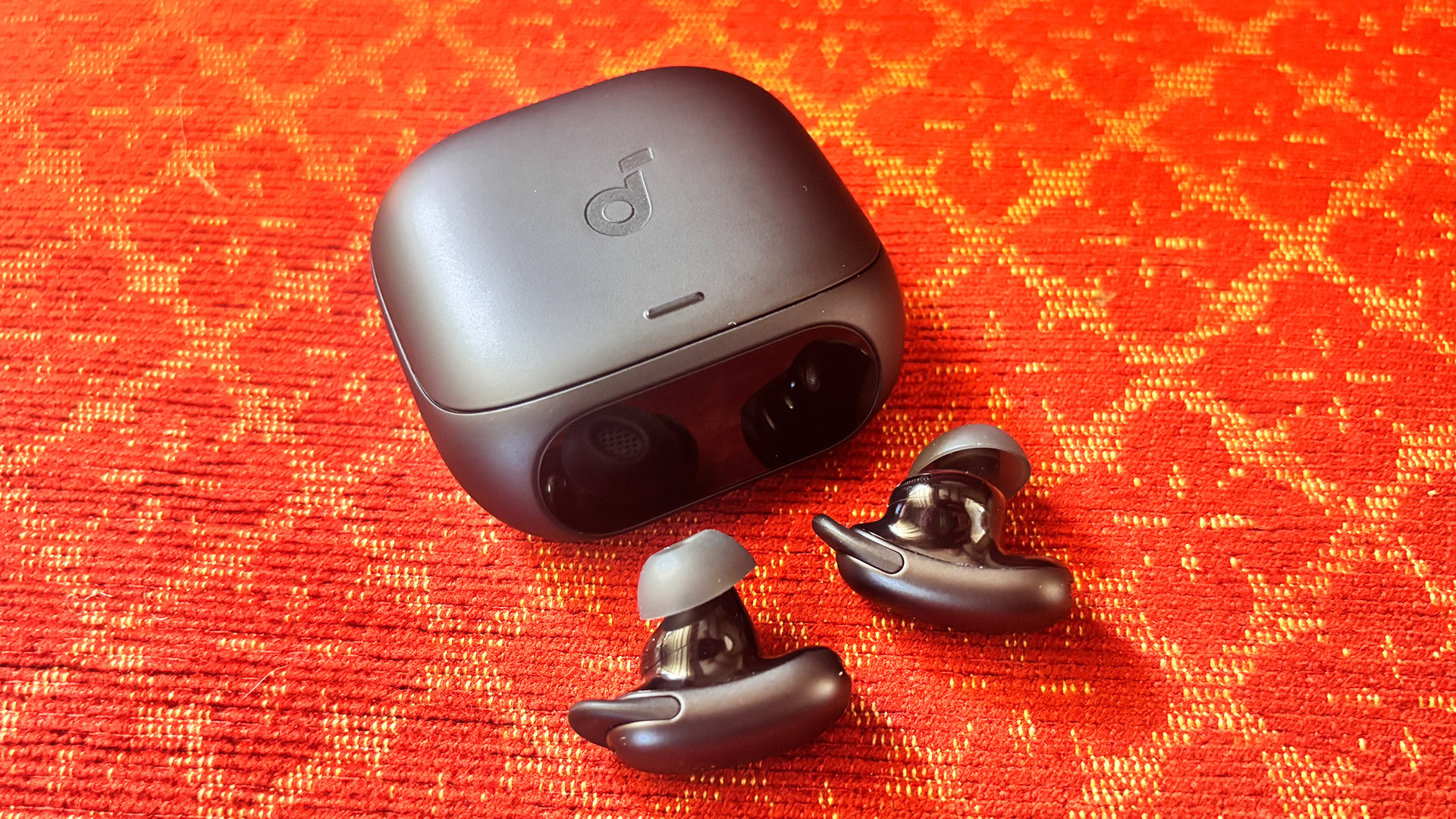 Soundcore Liberty 5 Pro in-ear headphones next to case on red and yellow patterned fabric