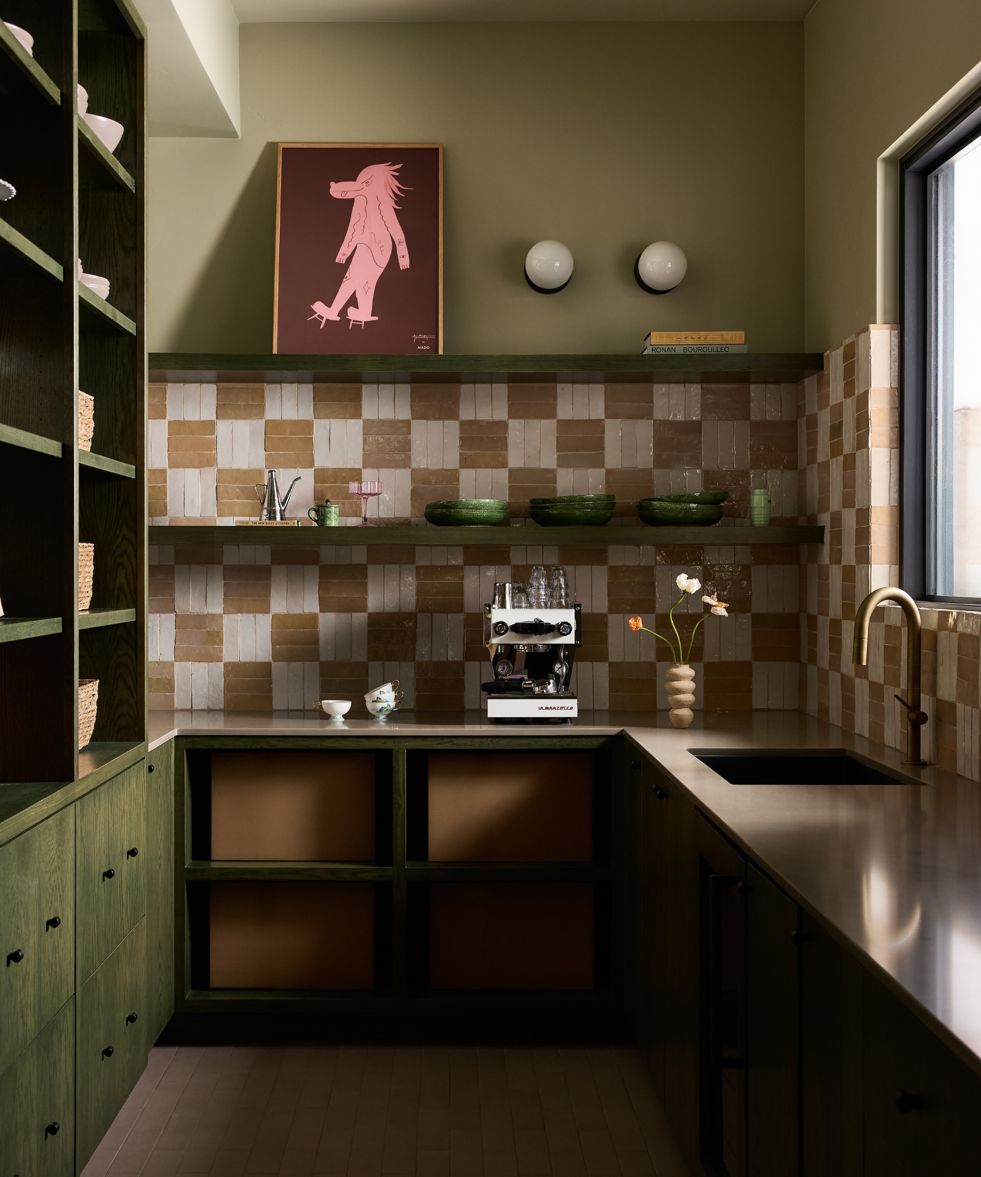 A walk-in pantry with green walls, green-stained cabinetry, white and brown checkerboard backsplash tiles, and open shelving