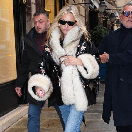 Kate Moss wears black sunglasses with a fur-trimmed coat.
