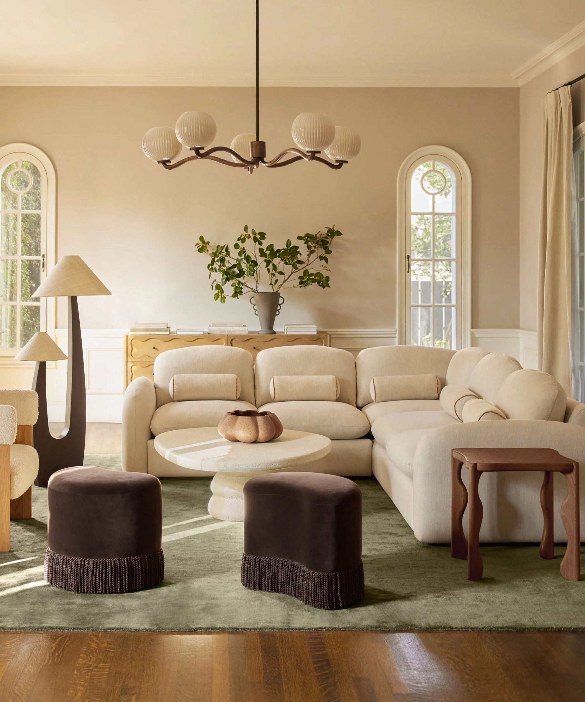 modern living room by lulu and georgia with a cloud like boucle modular sofa, soft green rug, dark plum purple ottomans with fringe tassel trim