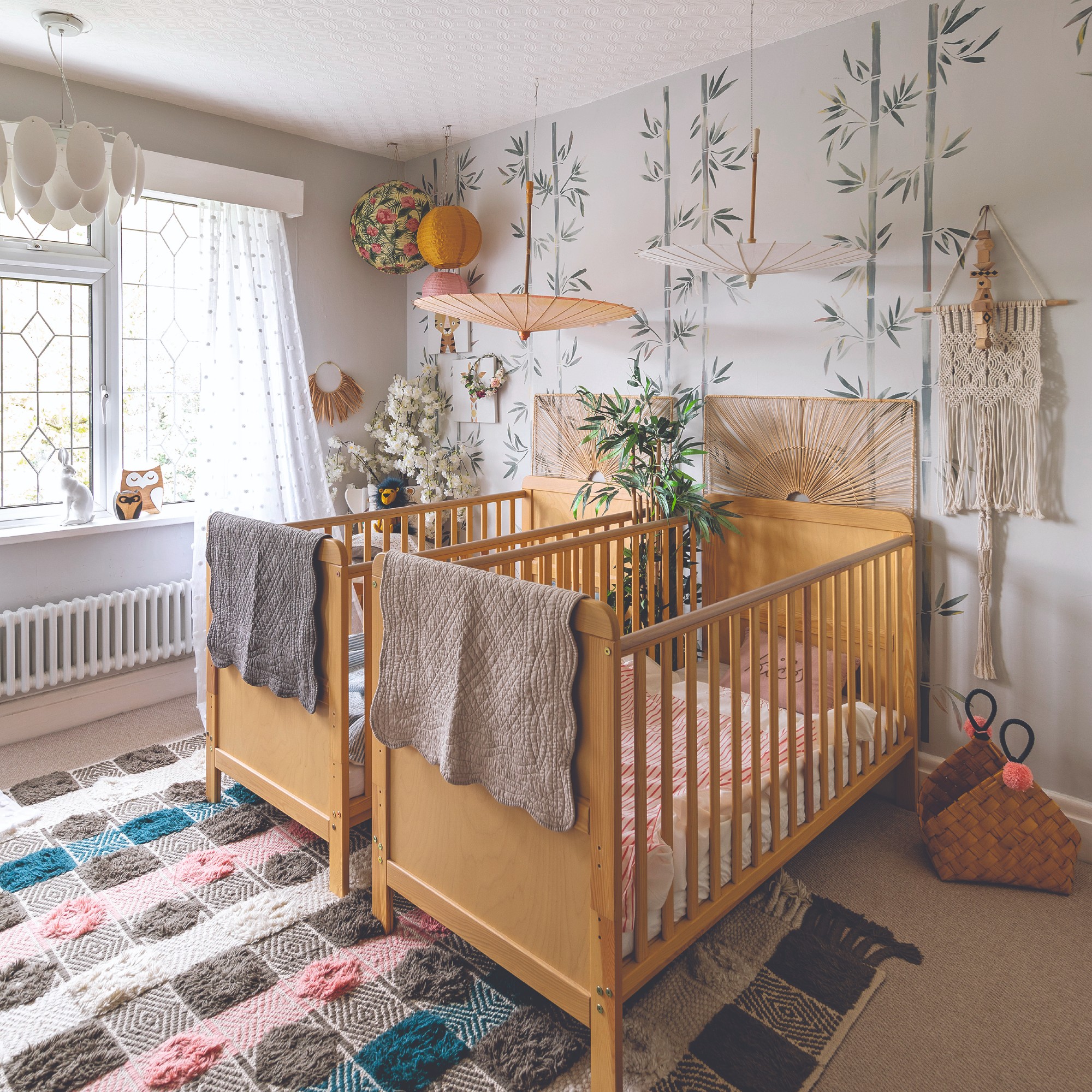 A nursery with two cots, lanterns and a bamboo-motif wallpaper on a feature wall