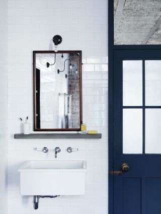 white bathroom with metro tiles, white basin, mirror, wall lights, blue door