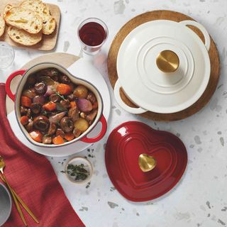 Aldi red and cream heart shaped cookware with cooked stew, baked bread and red tablecloth