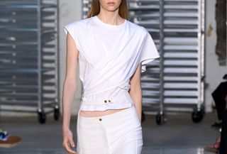 Model on a runway wearing a twisted white T-shirt.
