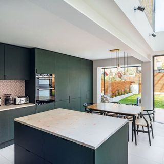 dark green kitchen with pink splashback and dining table