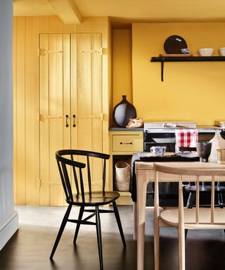 Yelllow kitchen with black chair, Aga and accessories, wood table, dark gray floor,