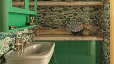 a green bathroom with a patterned wallpaper, a green gloss cabinet and a light green pedestal basin