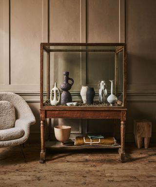 A wooden console table on a wooden floor against wood panelling with sculptural objects and vases displayed.