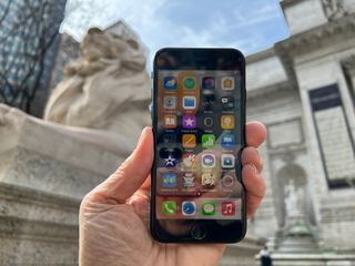 En hand håller upp en Apple iPhone SE framför en fontän.