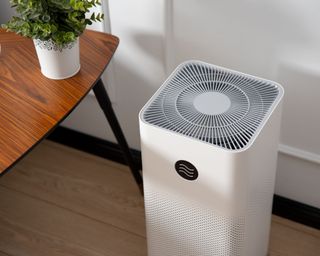 A white air purifier next to a wooden table with fake houseplant in white pot