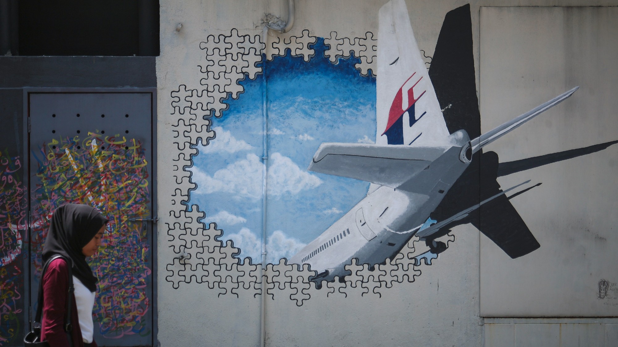 A woman walks past a mural of the missing Malaysia Airlines flight MH370 in Kuala Lumpur