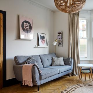 Living room with grey mid-century style sofa, picture ledges with framed prints, wooden herringbone parquet flooring and a nest of Scandi-style side tables