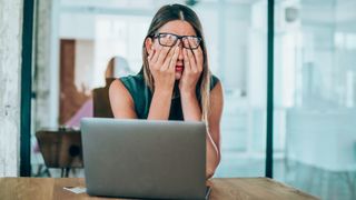 A woman rubbing her face in embarrassment in front of a laptop