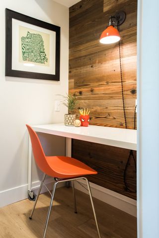 Home office with white console desk, orange chair, white wall and wood floor wood panelled wall and