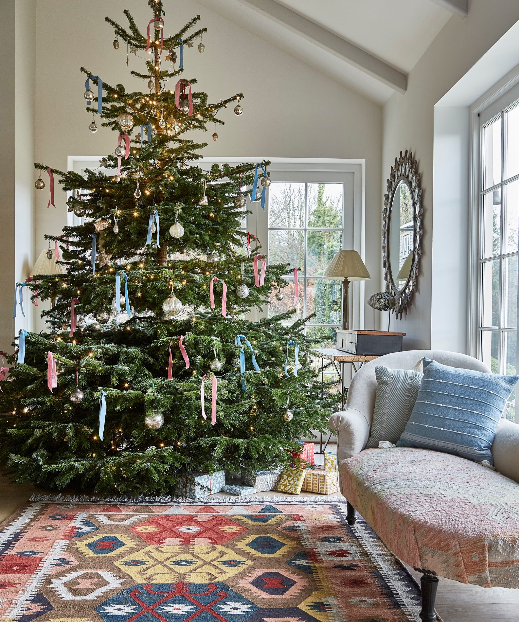 neutral living room with a large vintage style kilim rug, a chaise longue, and a large christmas tree styled with baubles and ribbons