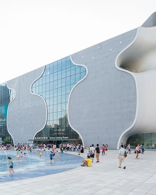 Exterior of National Taichung Theater with people paddling in a pool