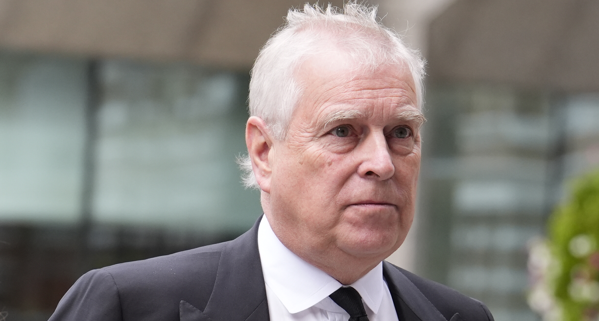 Prince Andrew wearing a suit and tie grimacing