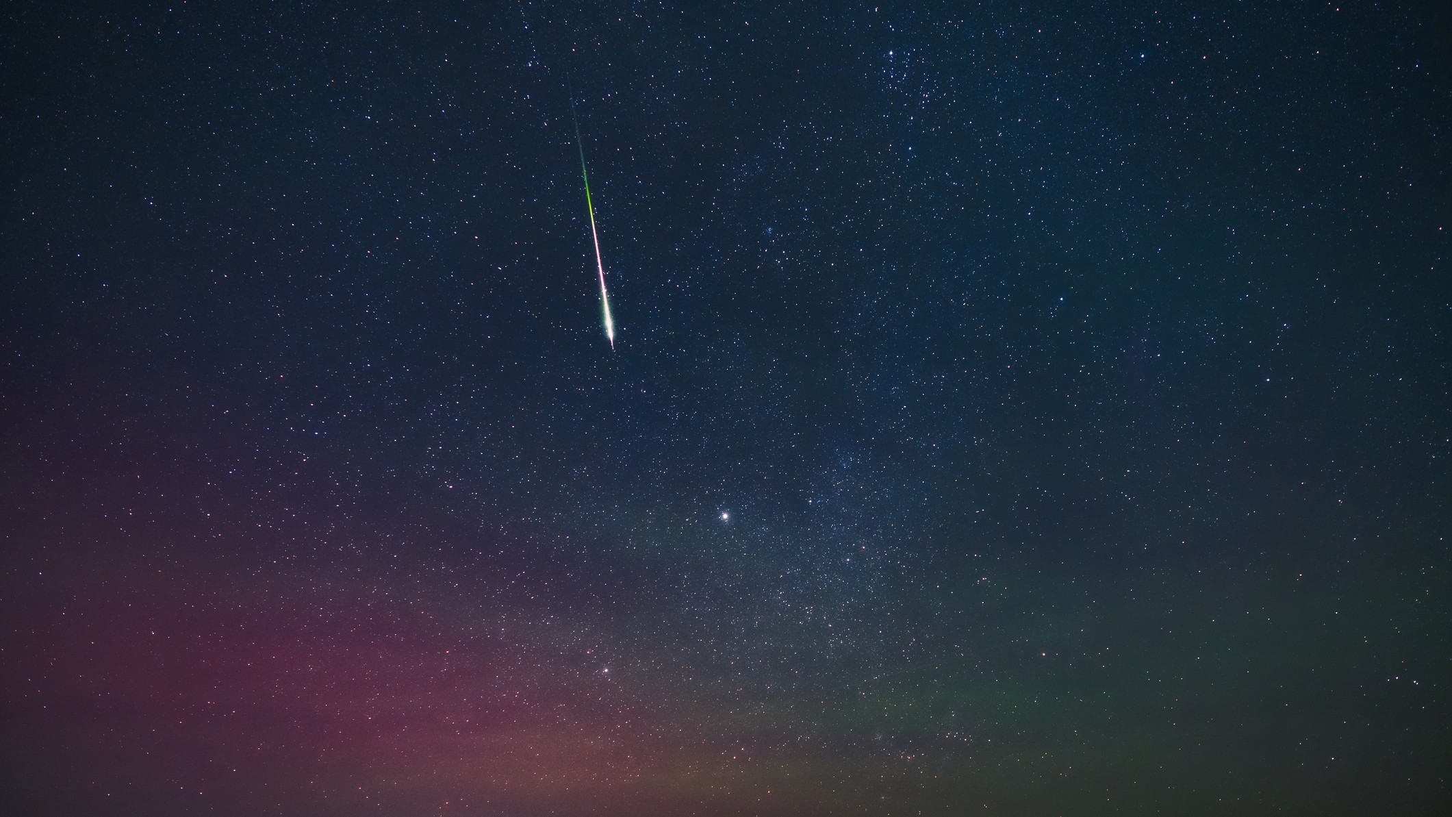 a meteor streaks through the sky in the center of the image. the sky glows red closer to the horizon.