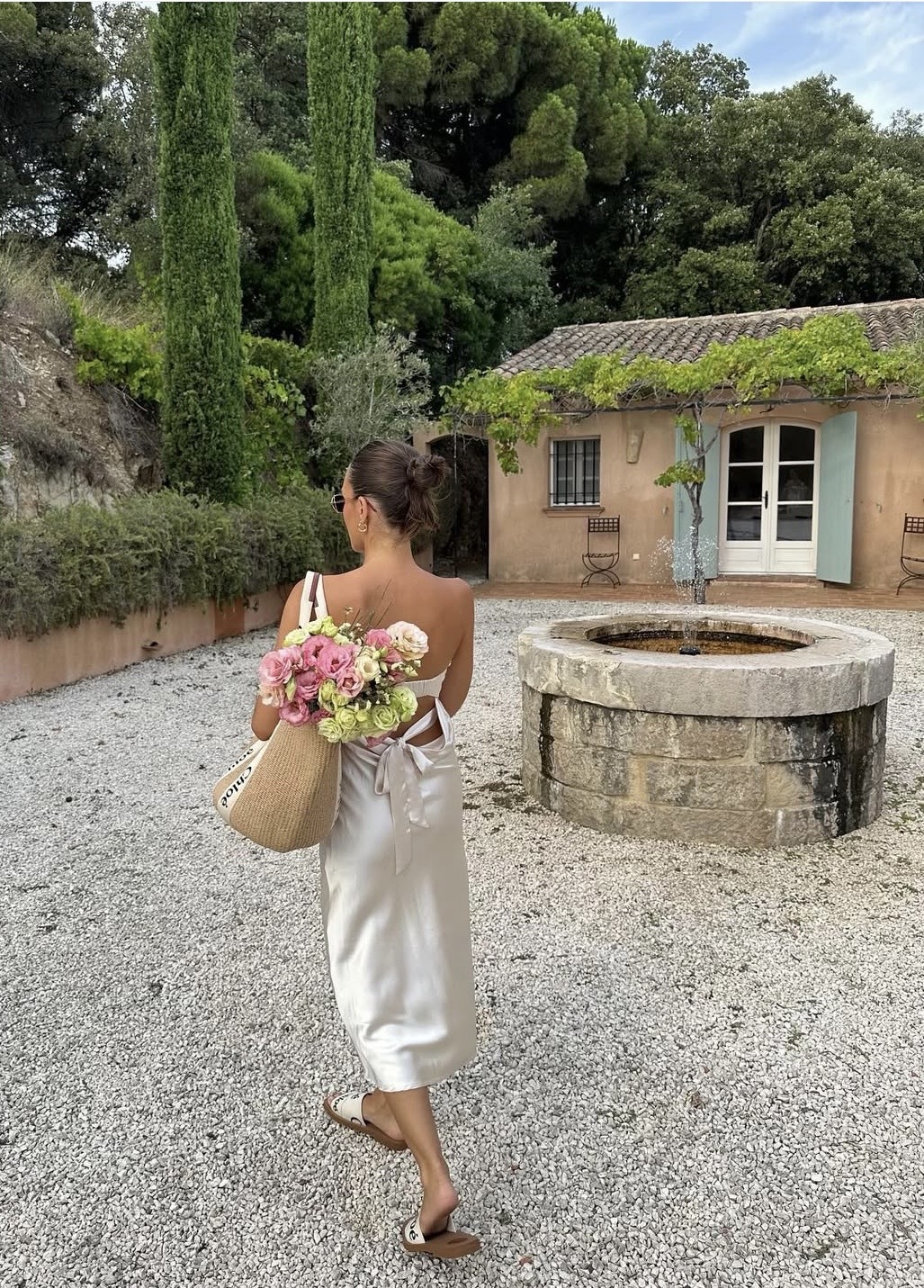 Influencer Emma Leger wears a silk midi dress, with a Chloe canvas sandal and Chloe raffia toe bag in a recent picture on her instagram in the South Of France.