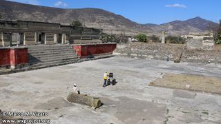 A man pushes a lawn-mower type instrument in a large stone courtyard.