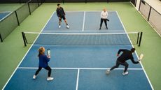 A group of four young adults play pickleball.