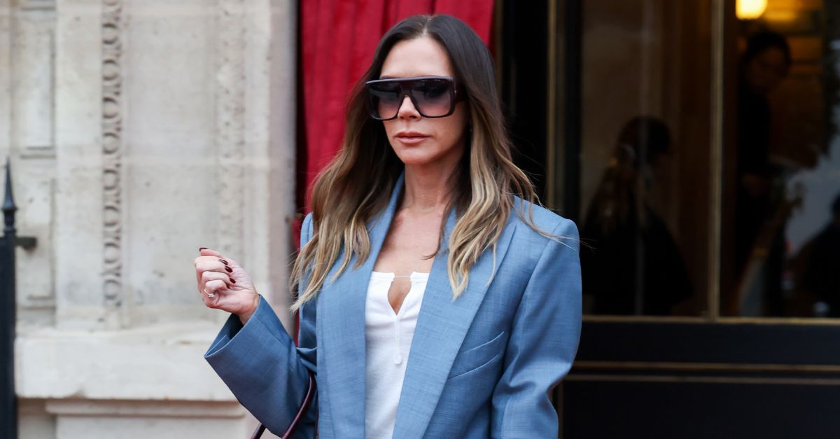 Victoria Beckham wears a light blue suit with a dark burgundy bag and large aviator sunglasses.