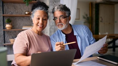 An older couple work on paperwork at their kitchen table.