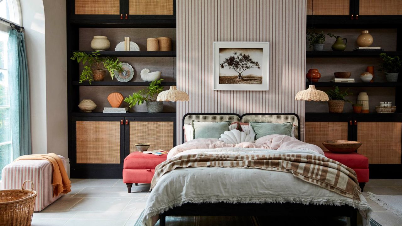 Modern organic bedroom with rattan shelves filled with objects, rattan bedframe with linen bedding and red ottoman side tables