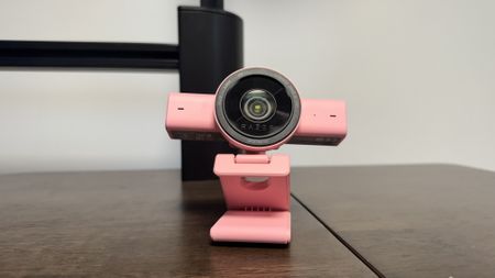 The pink Razer Kiyo V2 on a wooden desk, with the lens pointing to the centre and up
