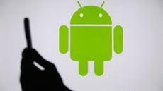 Android symbol in green displayed in background with person holding smartphone in foreground.
