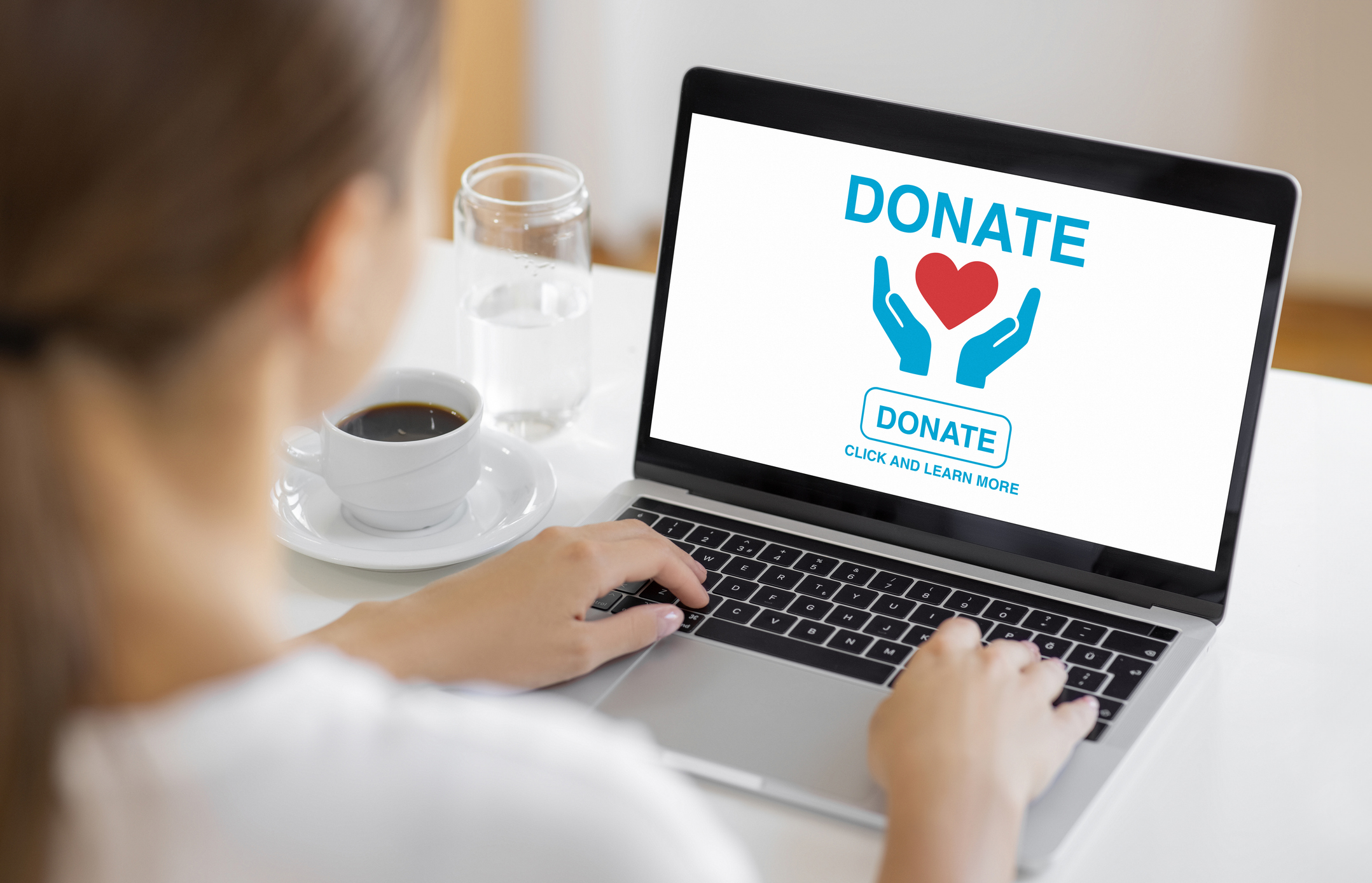 Woman using laptop with donation interface on screen showing heart and hands icons for charity support.