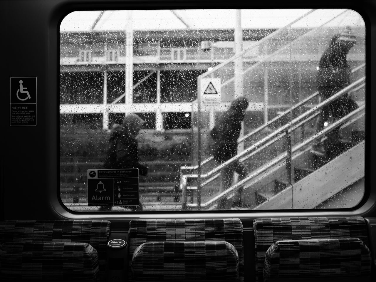 Mono image of pedestrians climbing stairs, shot through a rainy window on the OM System OM-3 with the OM System M.Zuiko 25mm f/1.8 II