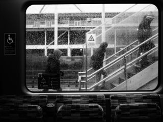 Mono image of pedestrians climbing stairs, shot through a rainy window on the OM System OM-3 with the OM System M.Zuiko 25mm f/1.8 II