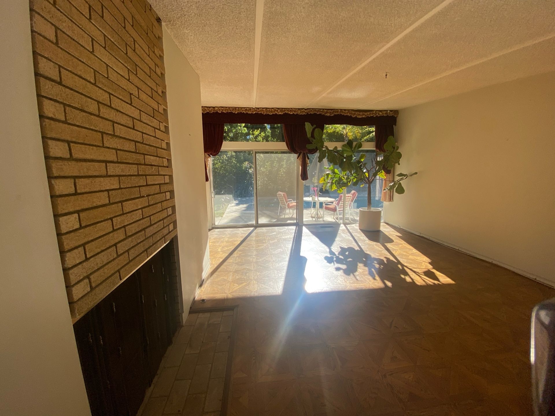 An open plan living room with large windows, a brick fireplace and parquet flooring