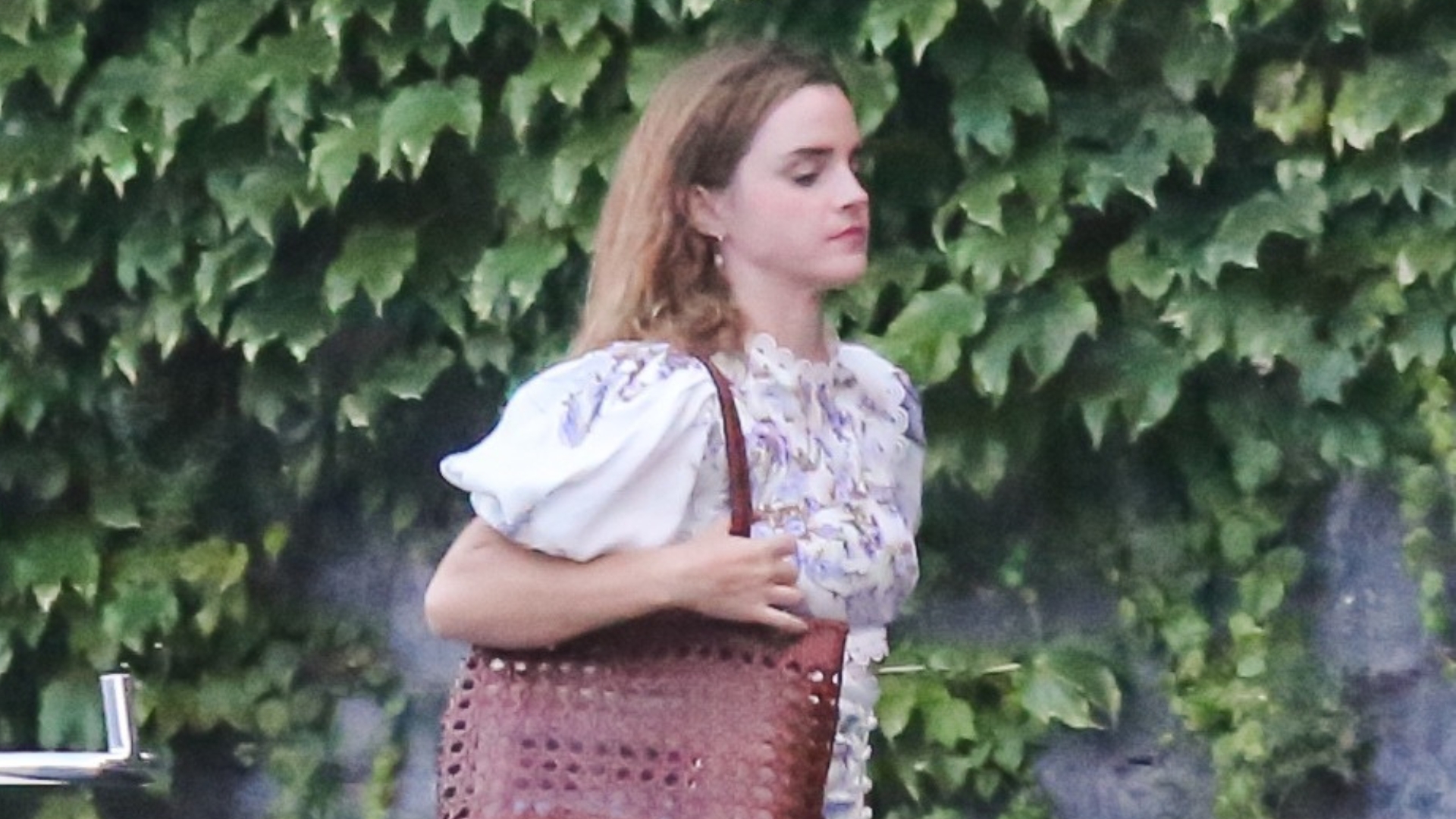 Emma Watson wears a while floral minidress with brown strappy sandals.