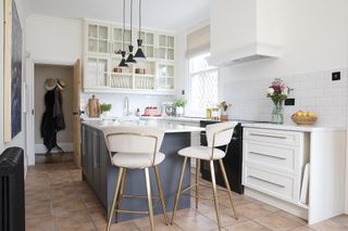 White Shaker-style kitchen with blue island, black pendant lights and pink and brass bar stools