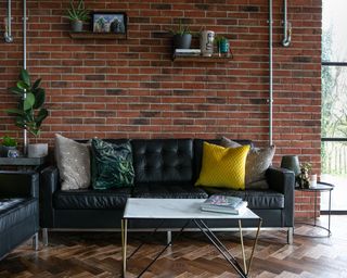A Victorian industrial style kitchen with living area with exposed brick wall and black leather sofa