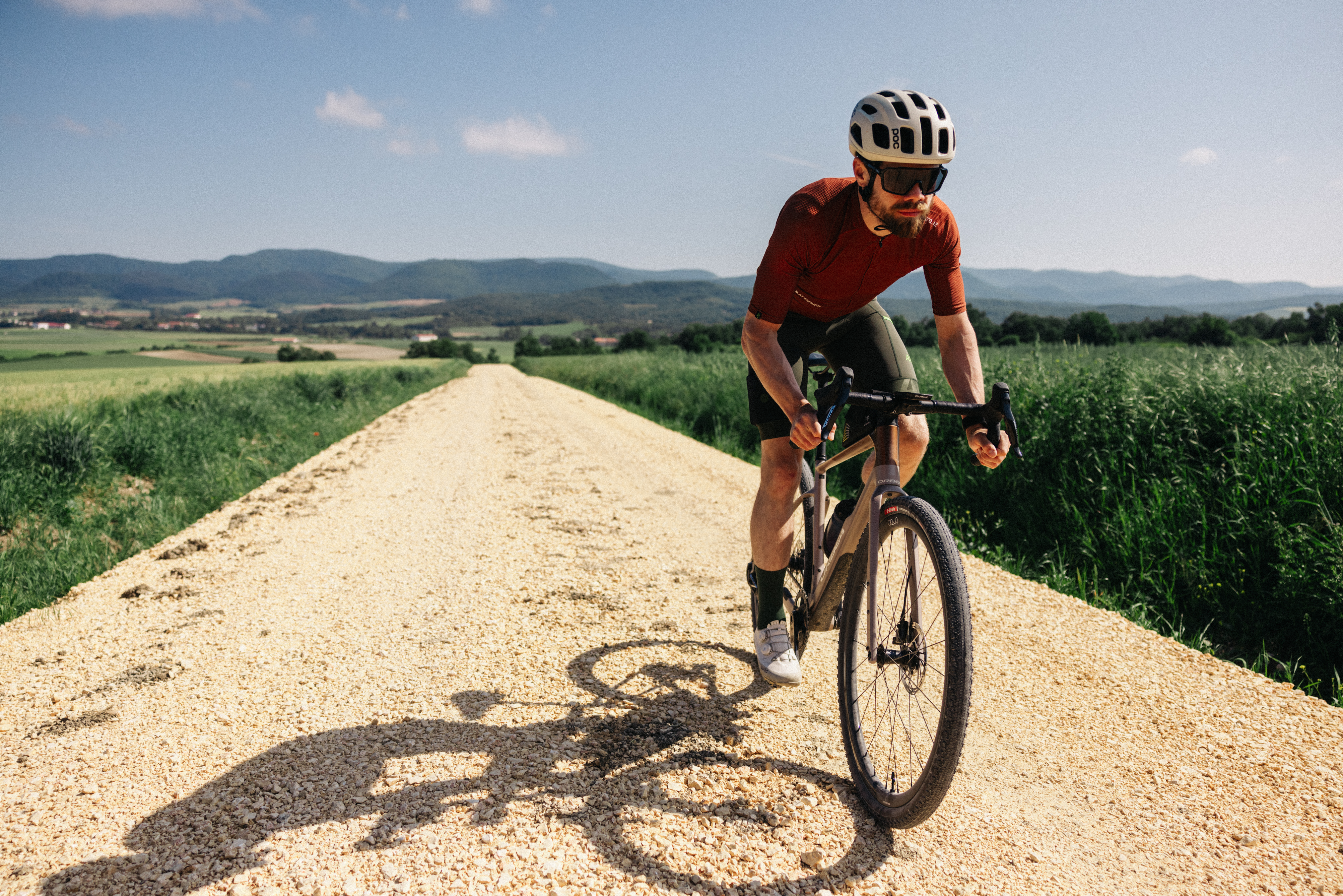 A man riding the new Orbea Terra on a gravel track between two fields