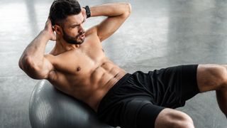 high angle view of young sportsman with bare chest doing abs exercise on fitness ball at gym