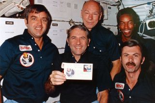 Space shuttle Challenger commander Richard Truly, floating in the orbiter's middeck, holds up one of the 10 envelopes, or covers, that he and his four STS-8 crewmates autographed while in orbit. Truly, a stamp collector, is finally receiving one of the collectibles after 38 years thanks to a fellow philatelist, David Ball.