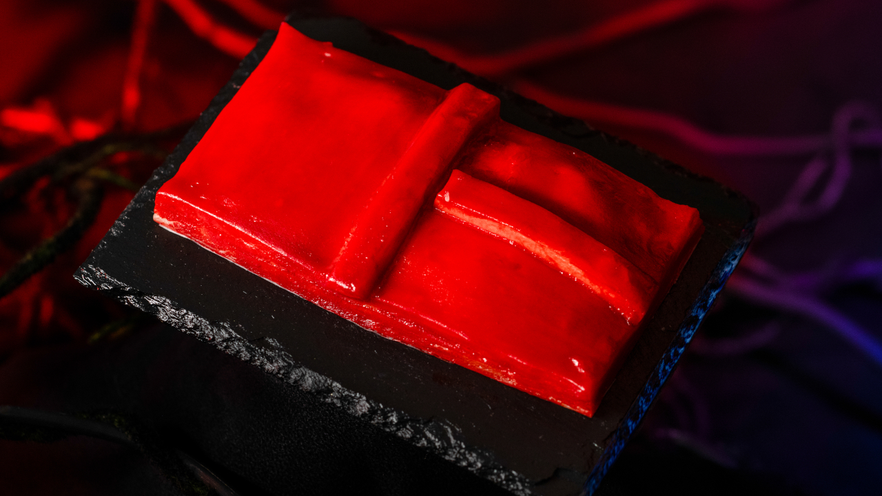 El pastel de mano de La Puerta Roja que se muestra servido sobre una mesa negra, frente a una cortina roja, de Universal Halloween Horror Nights 33.