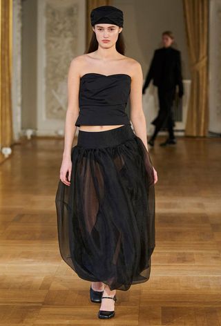 a model on The Garment fall runway wearing a black sheer ballon skirt with a strapless top