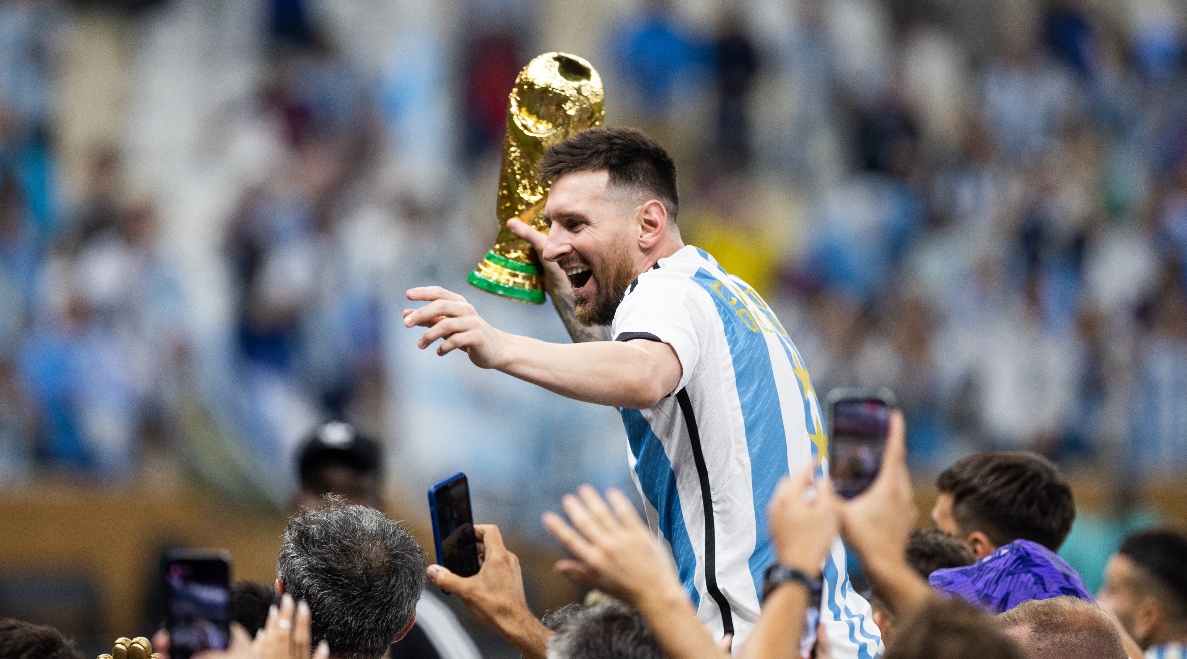 Lionel Messi of Argentina holds the World Cup trophy while being held aloft by teammates after Argentina beat France to win the FIFA World Cup 2022 on December 18, 2022 in Qatar.