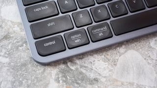 a black and grey budget wireless Bluetooth keyboard with a full-size layout and a numerical keypad is photographed against a blue background