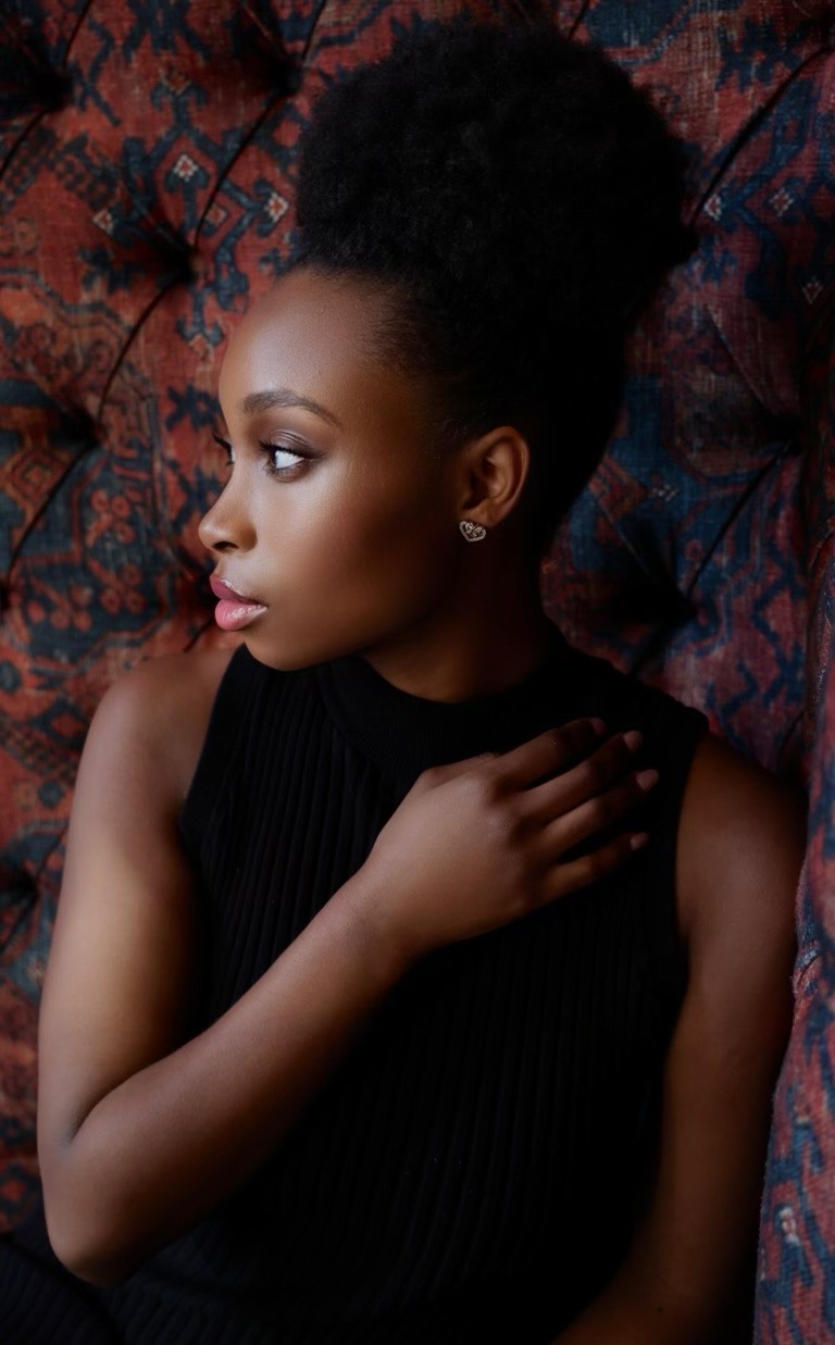 broadway actress nichelle lewis from ragtime poses in a black dress with a hand on her shoulder while sitting on an orange printed couch